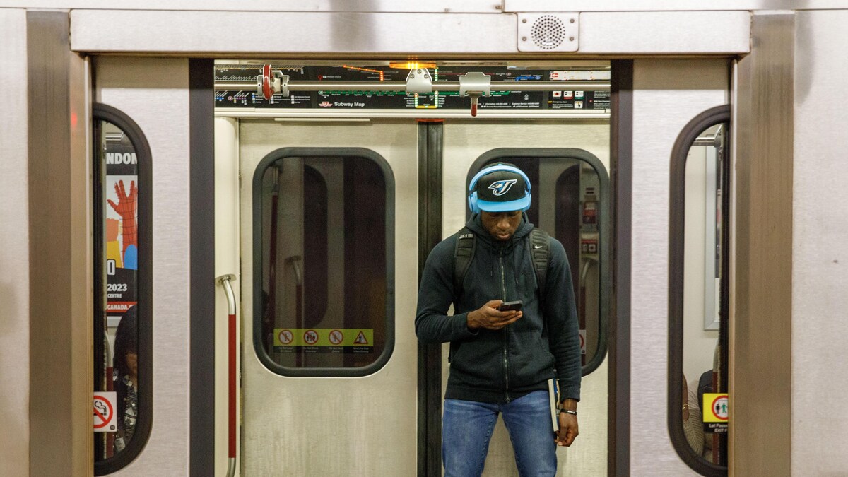 Un usager regarde son cellulaire à bord d'une rame de métro.