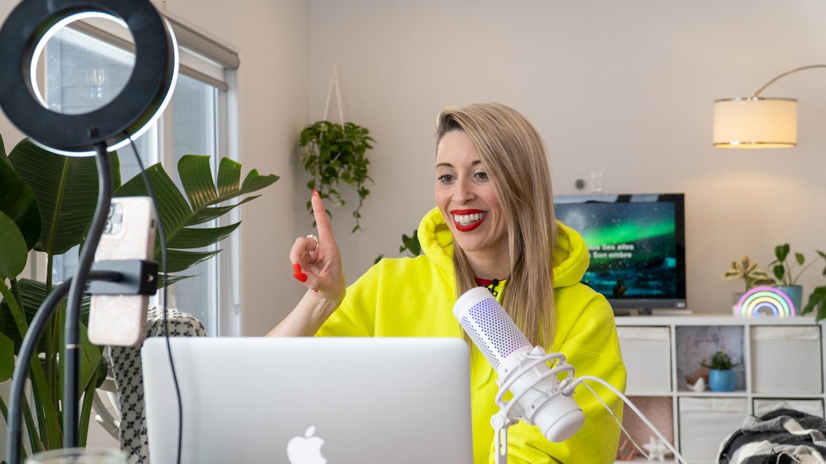 Une femme sourit en faisant un signe de la main devant un ordinateur.