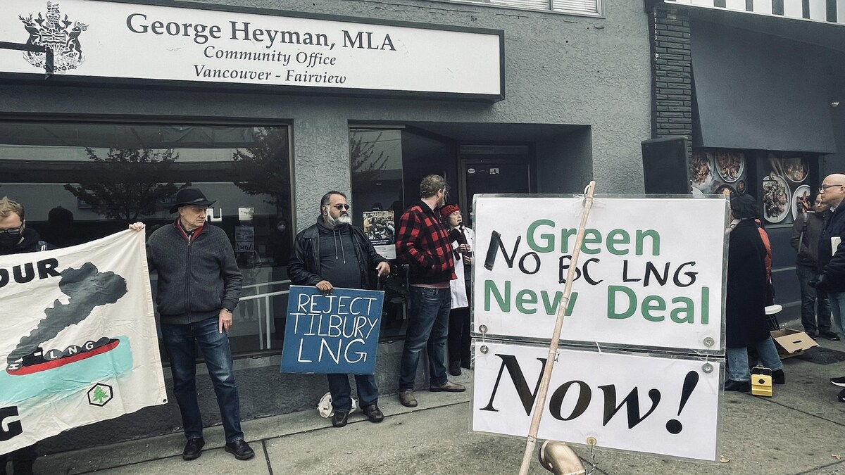 Des gens qui tiennent des pancartes avec des slogans contre le projet de gaz naturel liquéfié sont debout devant l'immeuble du ministre George Heyman.