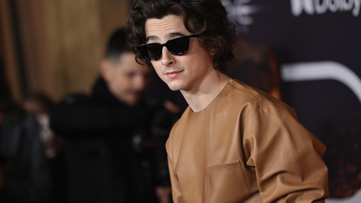 L'acteur vêtu de cuir beige avec des lunettes de soleil opaques.