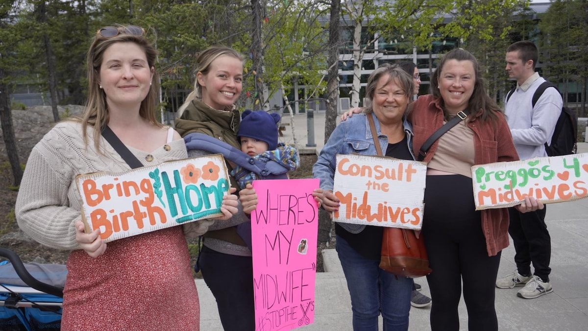 Quatre femmes se tiennent côte à côte et en tenant des pancartes colorées dans leurs mains, le 20 mai 2024, à Yellowknife, aux Territoires du Nord-Ouest.