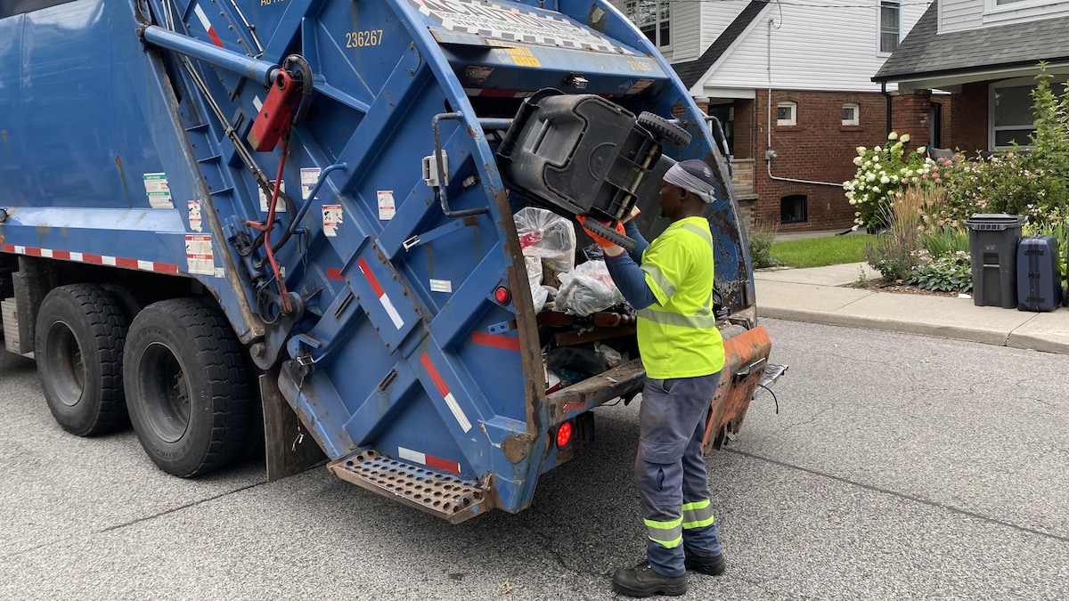 Un éboueur vide le contenu d'une poubelle dans un camion d'ordures.