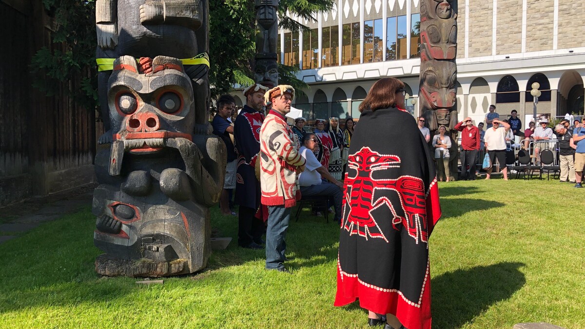 Des représentants de Premières Nations de l'île de Vancouver s'adressent au public au pied de totems.