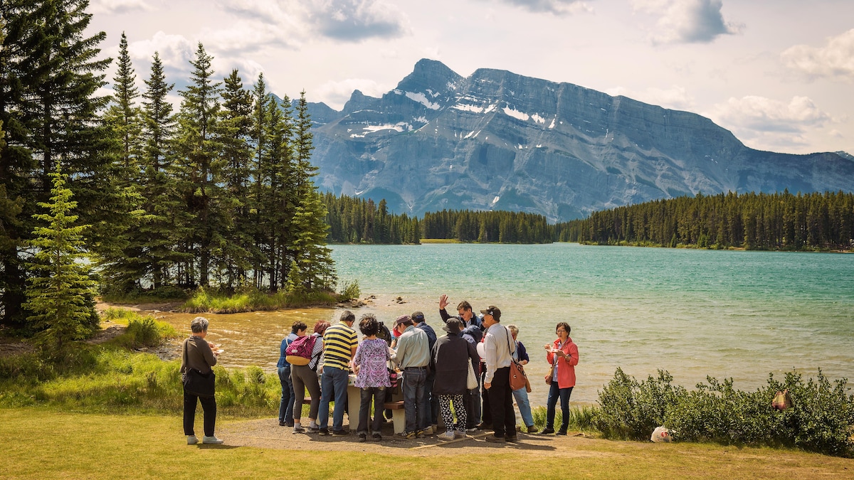 Des touristes asiatiques visitent le parc national de Banff. Ils se tiennent devant le lac Two Jack. Au loin s'élève le mont Rundle.