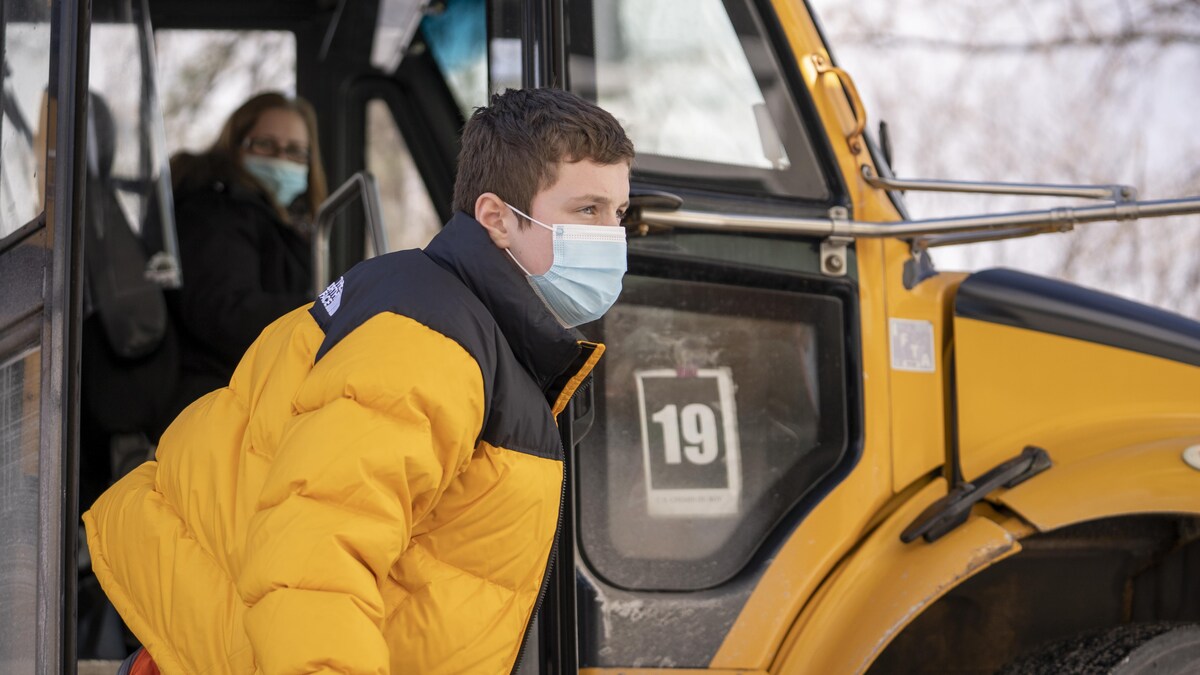 Un élève masqué sort d'un autobus scolaire.