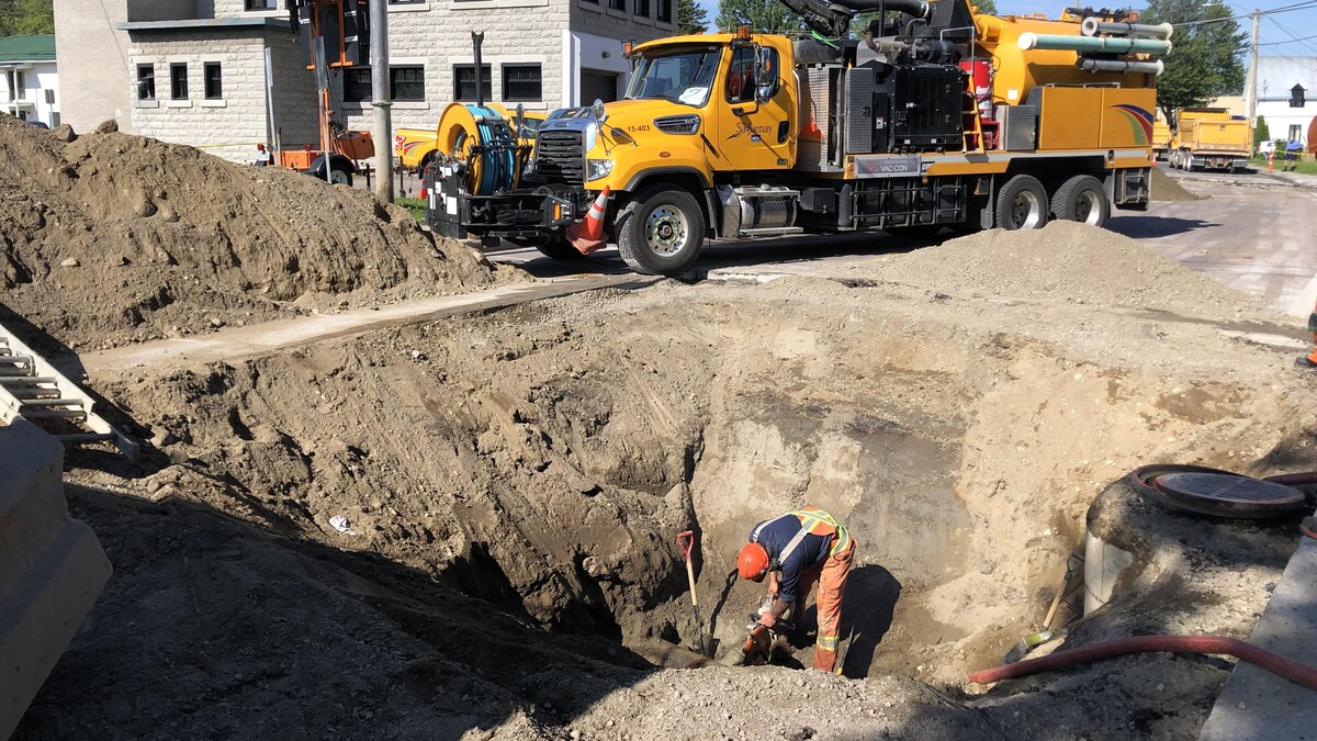 Un travailleur s'affaire dans un trou creusé par une pelle mécanique.
