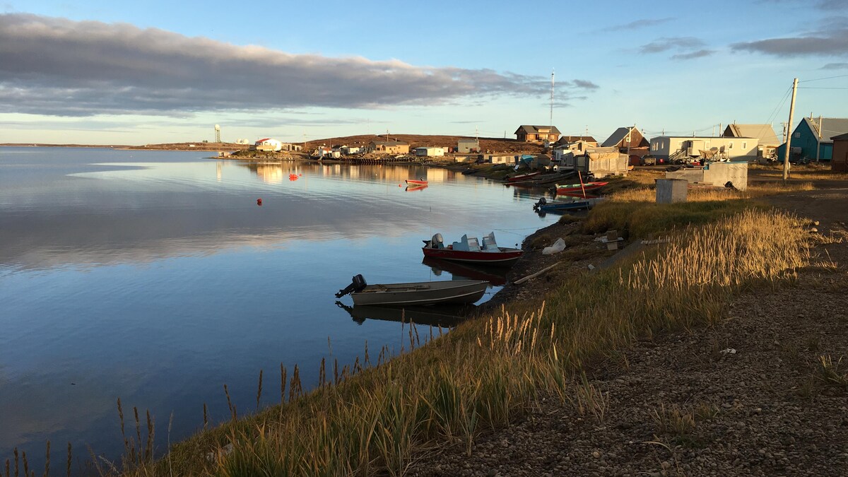 Vue sur village de Tuktoyaktuk, sur le bord de l'eau, dans le grand nord canadien. Des maisons et des chaloupes bordent la rive.