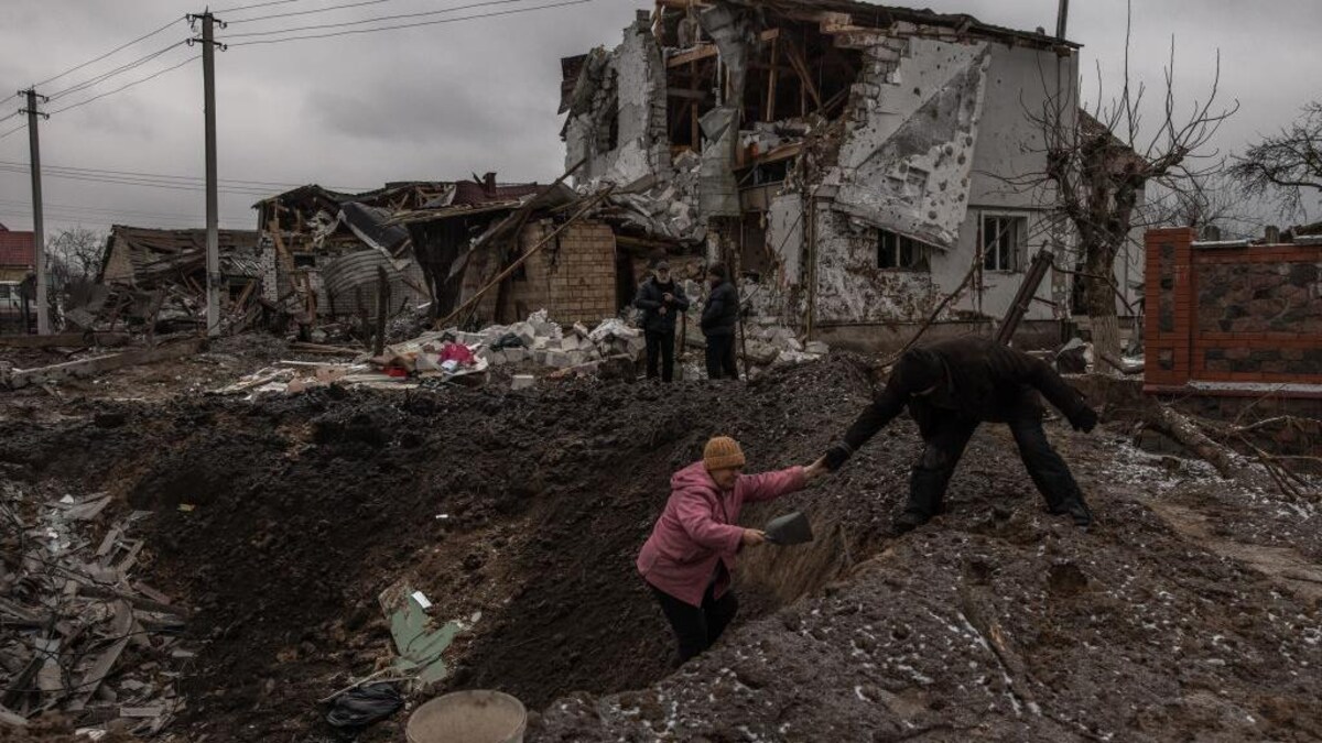Un homme aidant une femme à sortir d'un cratère après un bombardement russe dans la région de Kiev.