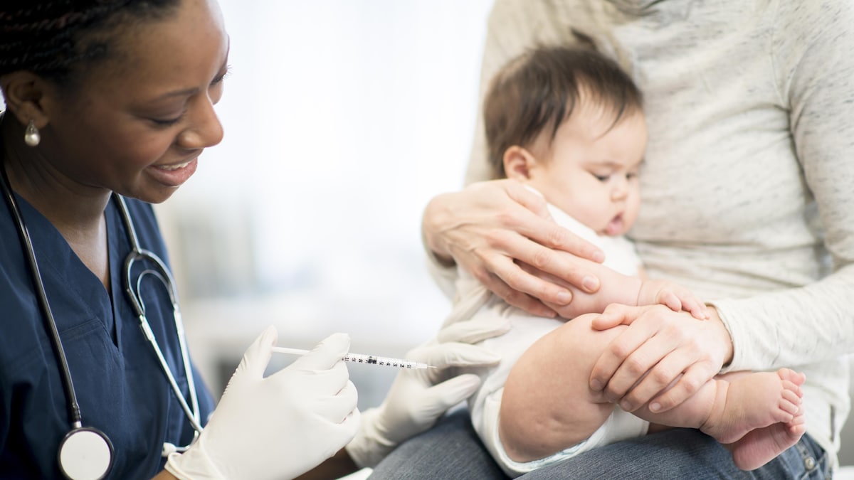 Un jeune enfant dans les bras de sa mère est sur le point de recevoir un vaccin.