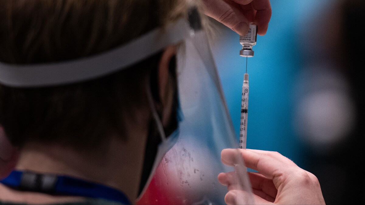 Une infirmière insère une aiguille dans une fiole de vaccin.