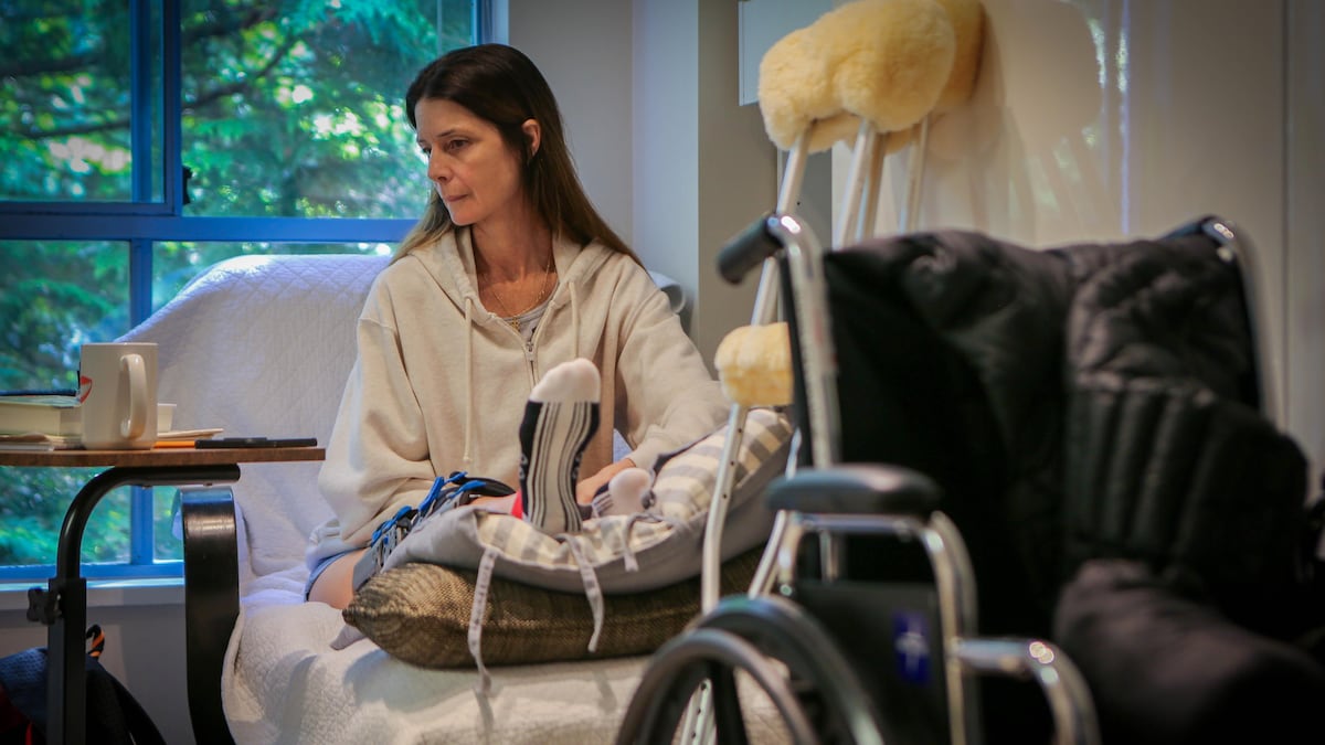Valérie est allongée sur un fauteuil, la jambe surélevée, avec en premier plan un fauteuil roulant et des béquilles.