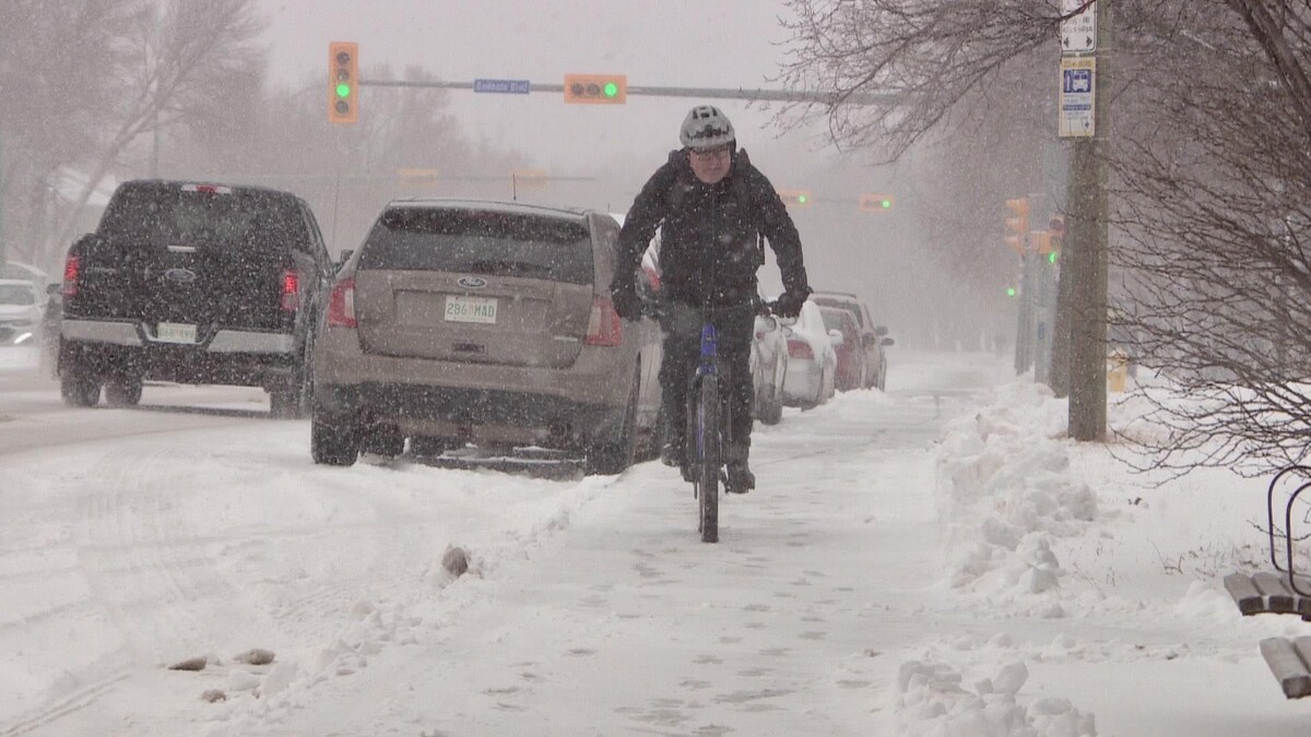 Un homme en vélo lors d'une tempête de neige printanière s'abat à Regina, en Saskatchewan, le 19 avril 2023.