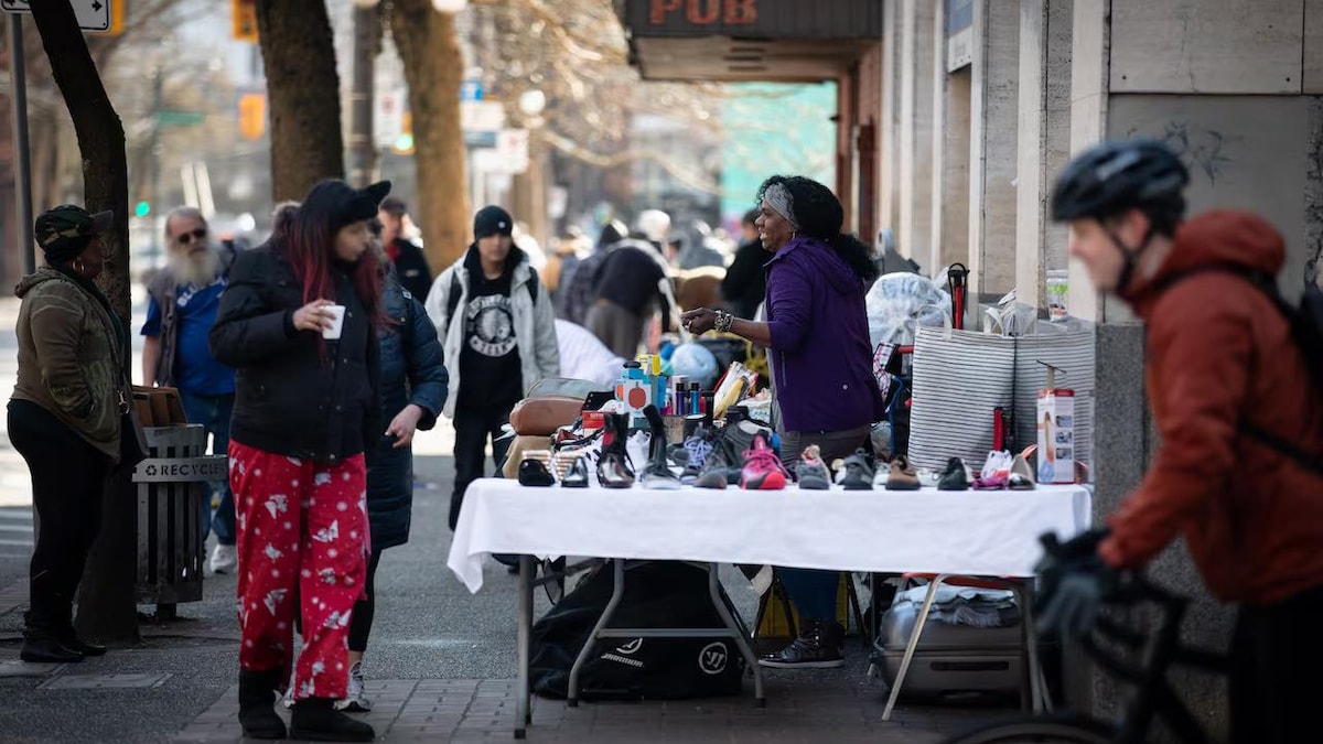 Une exposante qui vend des chaussures disposées sur une table installée sur un trottoir. 