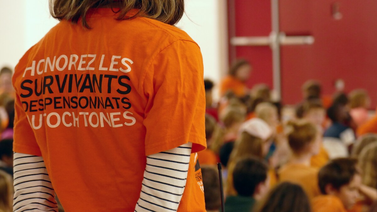 Une personne portant un chandail orange. Des enfants en arrière-plan.