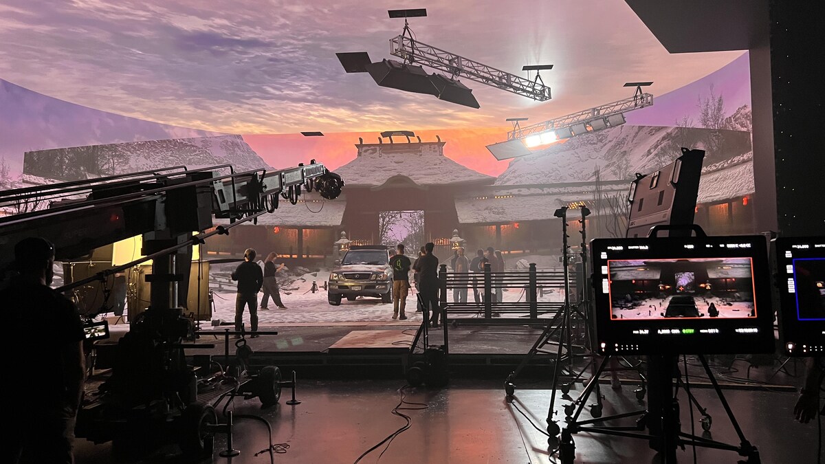 Un plateau de tournage intérieur avec des machinistes et une image de temple japonais sous la neige projeté sur un immense écran.