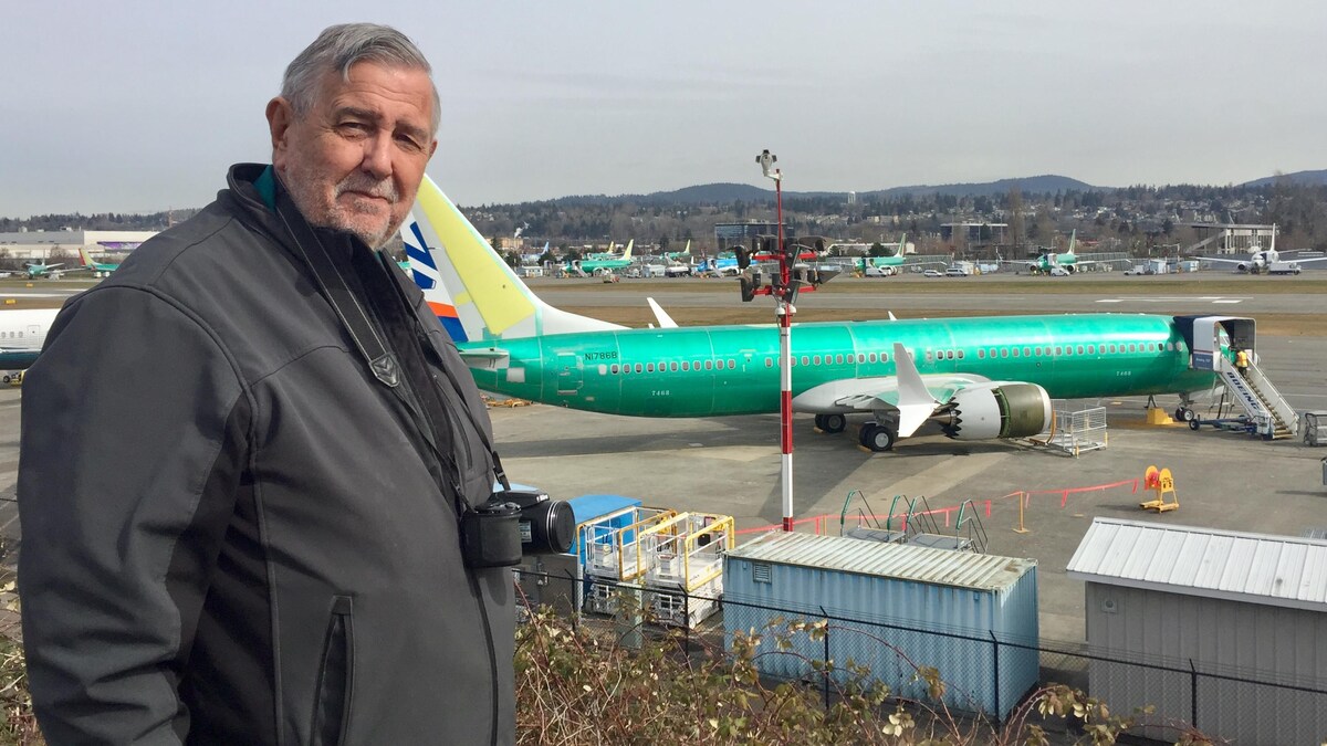 Un homme muni d'un appareil photo pose devant un tarmac sur lequel est posé un avion 737 MAX 8.