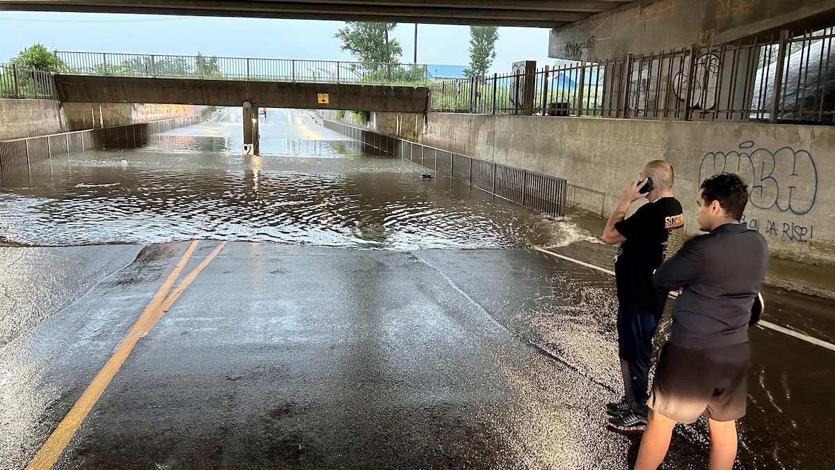 Deux hommes au téléphone devant une voiture submergée.