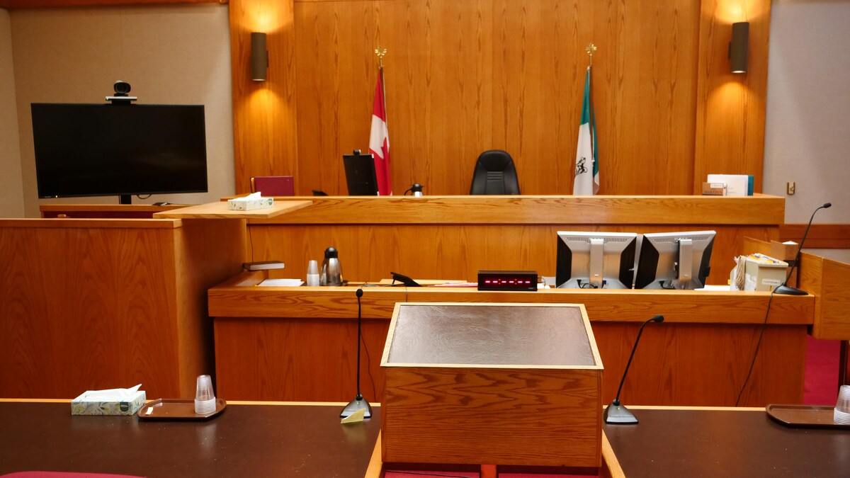 Salle d'audience vide d'un tribunal aménagée de bois avec un écran et une caméra dans un coin.