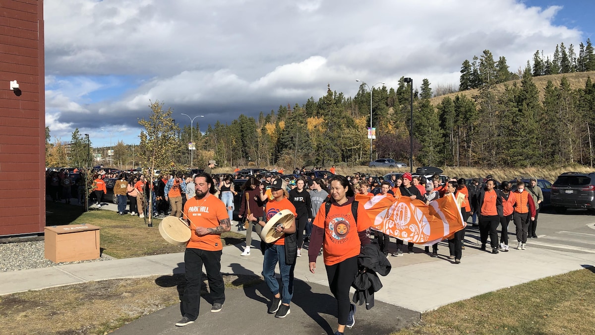 Groupe de jeunes qui marchent, vêtus de chandail orange et tenant des tambours.