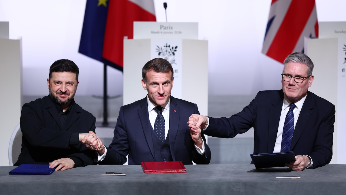 Volodymyr Zelensky, Emmanuel Macron et Keir Starmer, assis côte à côte derrière une grande table, se serrent les mains après avoir signé un document officiel.