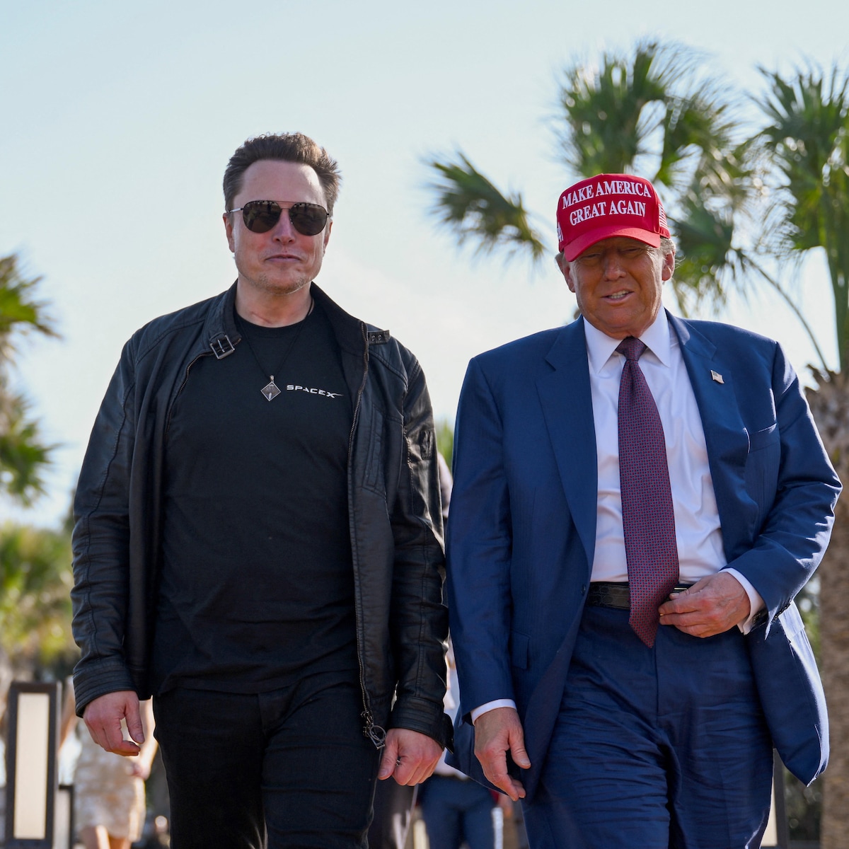 Elon Musk, qui porte des lunettes fumées, et Donald Trump, qui porte une casquette rouge disant « Rendons sa grandeur à l'Amérique », marchent l'un à côté de l'autre. 