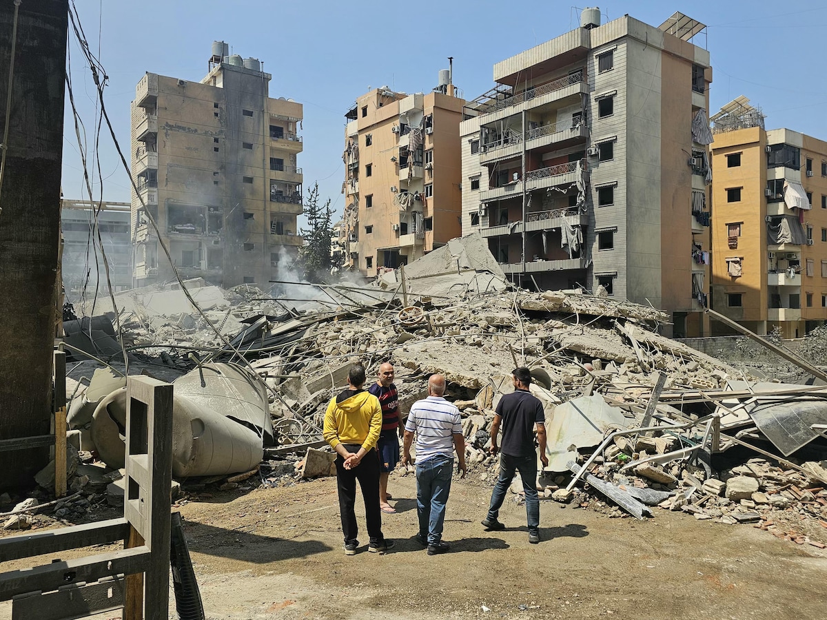 Des hommes discutent près de ruines encore fumantes.
