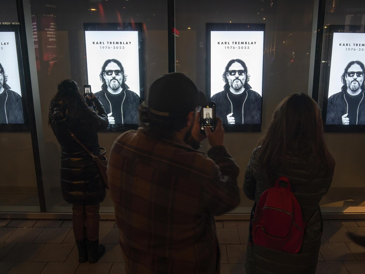 Quelques personnes prennent en photo quatre affiches montrant le chanteur Karl Tremblay. 