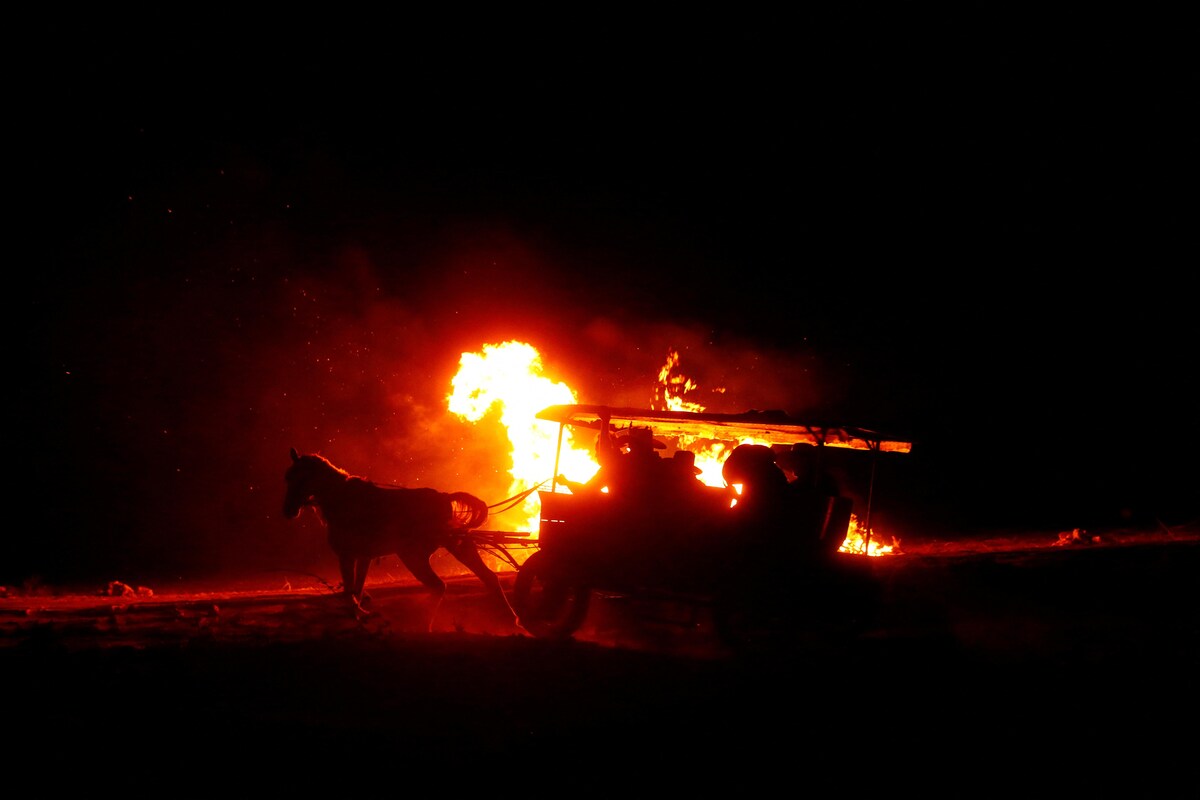 Une carriole tirée par un cheval roule la nuit et passe devant des arbres en feu.