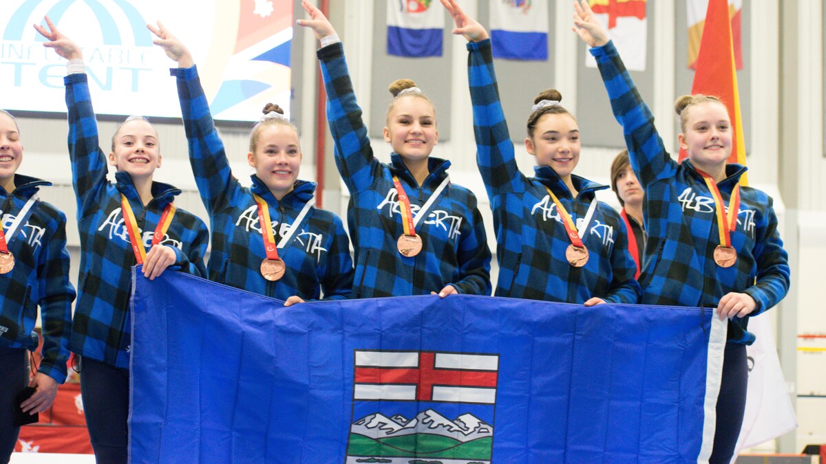 Une groupe de filles sur le podium, un bras dans les airs, avec un drapeau de l'Alberta. 