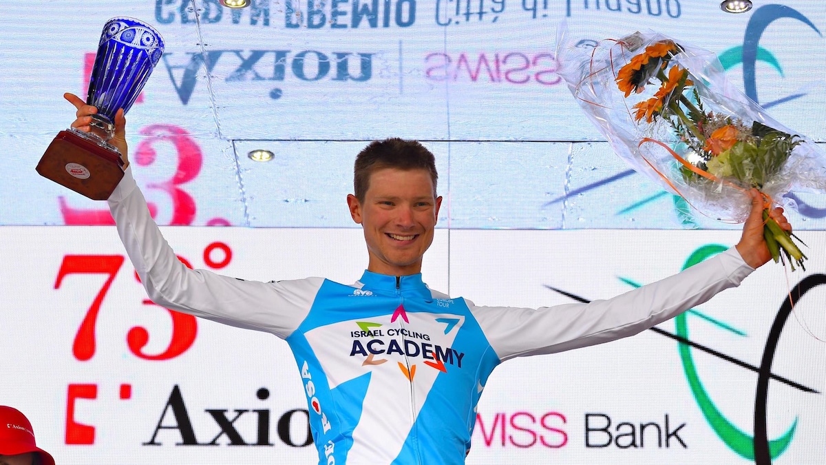 Sur le podium, il lève les bras avec un trophée dans la main droite et un bouquet de fleurs dans la main gauche. 