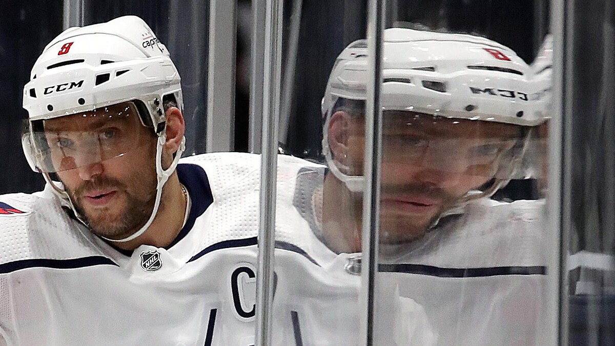Il entre sur la patinoire pour un match. On voit le reflet de sa tête dans la baie vitrée.