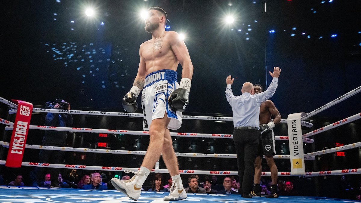 Un boxeur avec des shorts blanches et bleues retourne dans son coin après avoir stoppé son adversaire lors d'un combat professionnel.