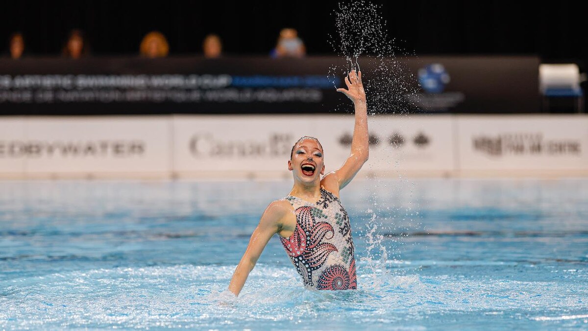 La nageuse artistique sort une main de l'eau en souriant.