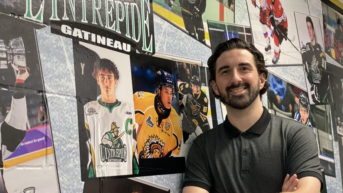 Un entraîneur de hockey prend la pose devant un mur célébrant les anciennes vedettes de son équipe.