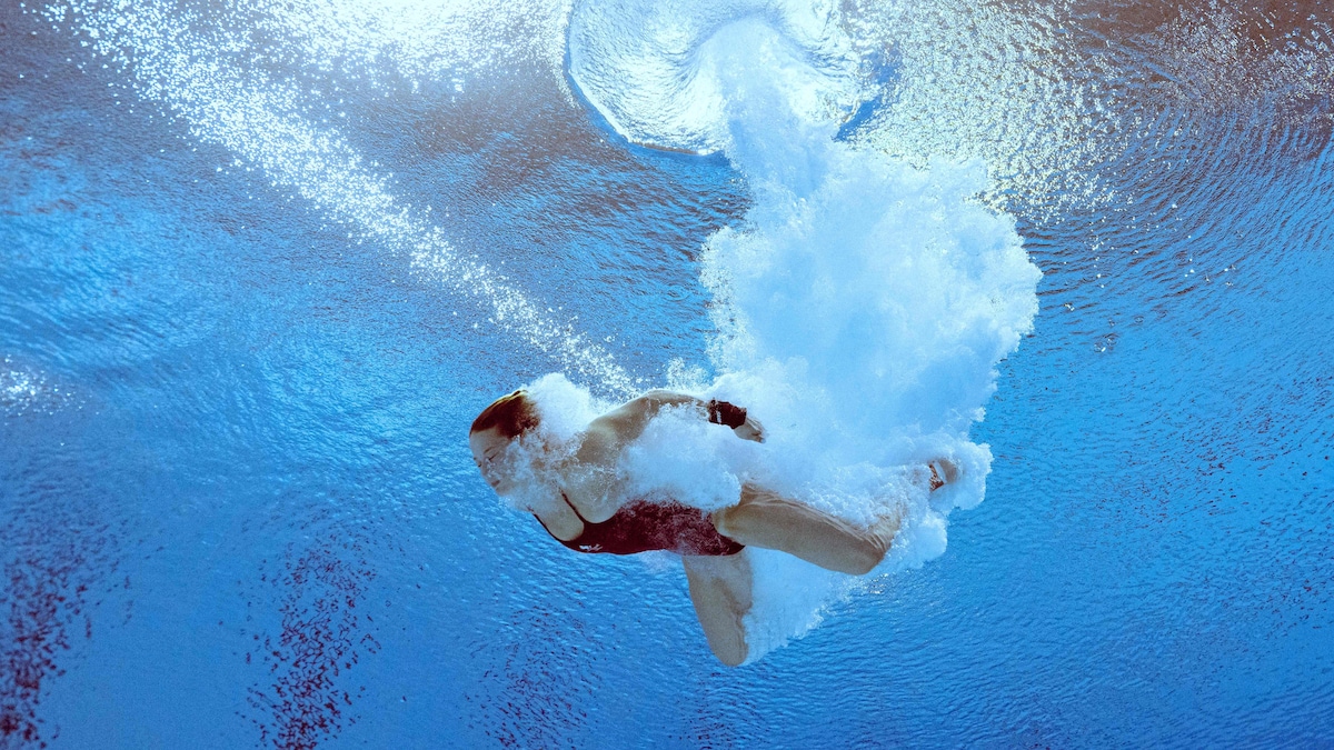 Une vue sous l'eau d'une plongeuse à son entrée dans la piscine