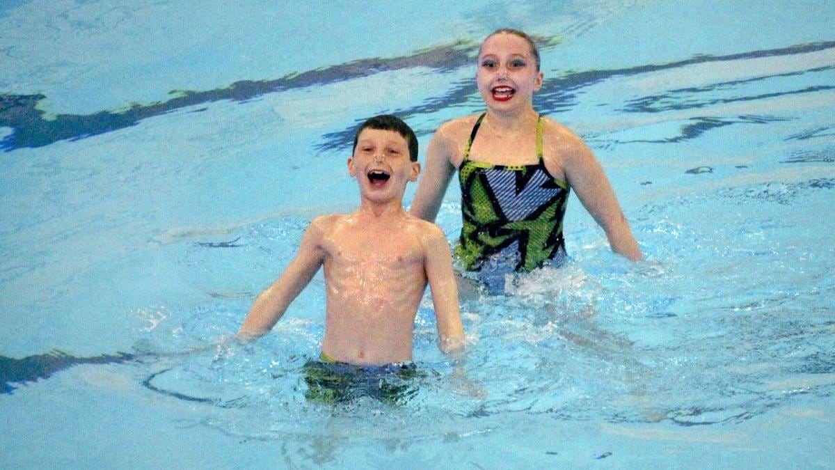 Un jeune nageur artistique et sa partenaire derrière lui font une routine dans une piscine.