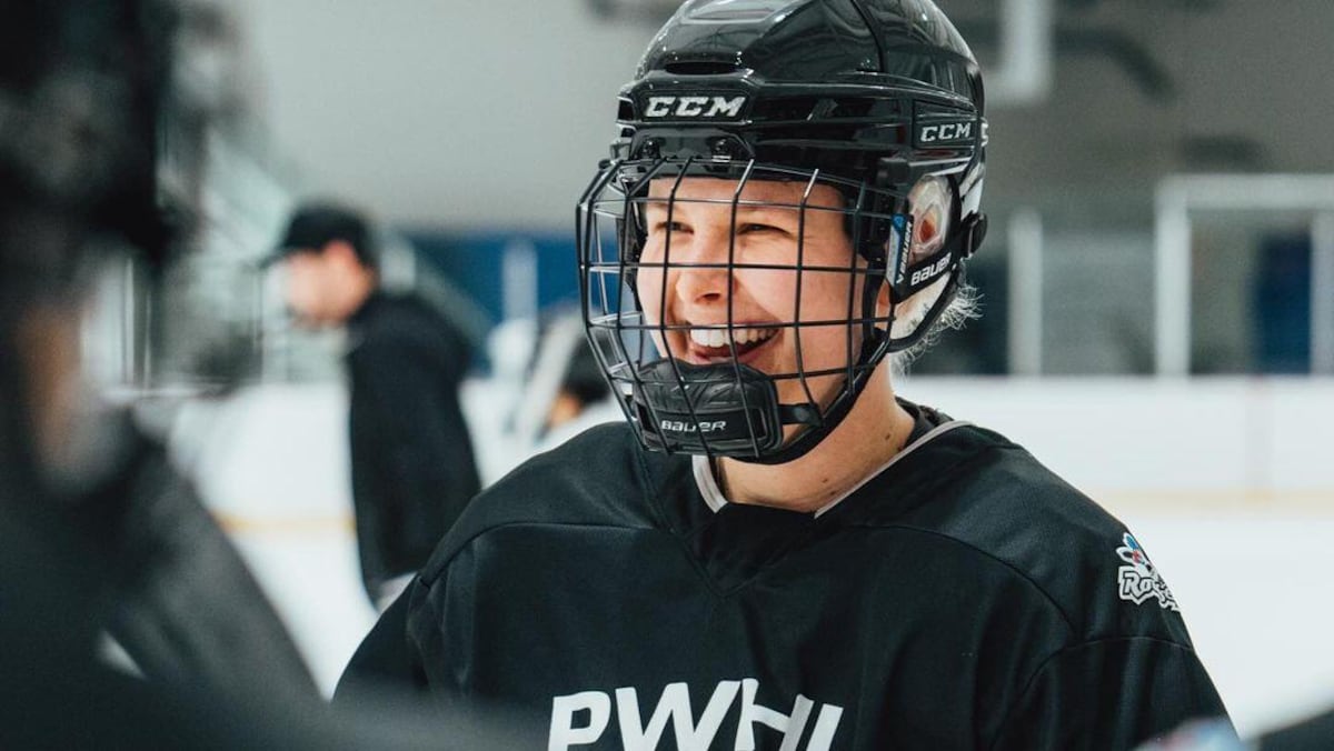 Une joueuse de hockey sourit sous son casque. 