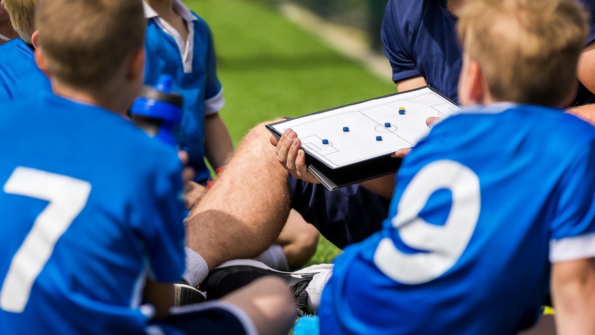 Des enfants sont accroupis et écoutent les conseils de leur entraîneur de soccer.