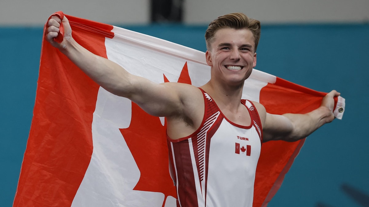 Le gymnaste Félix Dolci pose pour les photagraphes en brandissant le drapeau canadien derrière ses épaules.