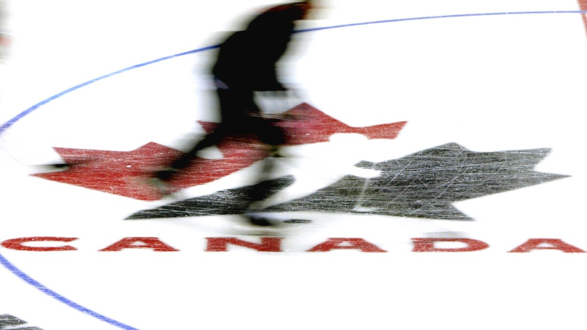 Une silhouette survole le logo de Hockey Canada incrusté dans la glace d'une patinoire.