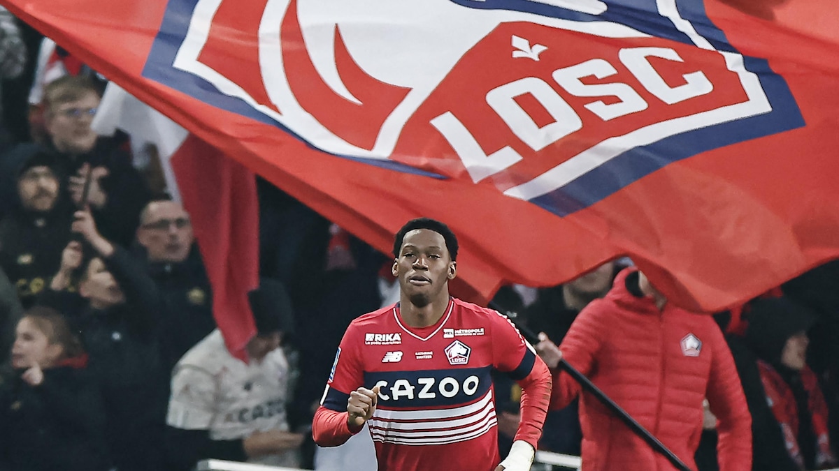 Un joueur de soccer sur le terrain, à l'arrière des spectateurs brandissent un immense drapeau avec le logo du club.