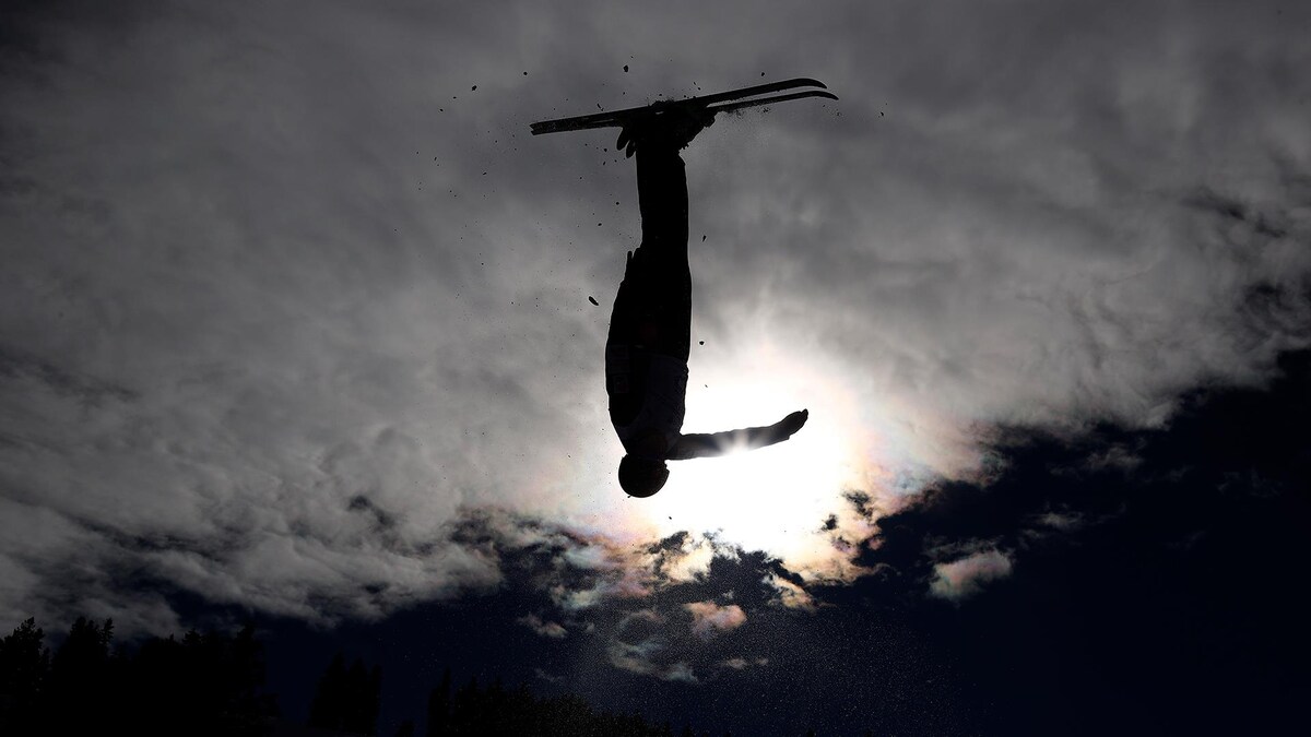 Une skieuse acrobatique à l'envers dans les airs.