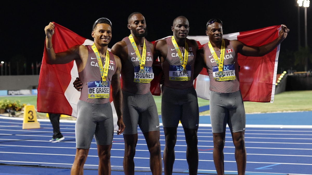 Quatre coureurs posent avec leur médaille au cou et tiennent des drapeaux du Canada.