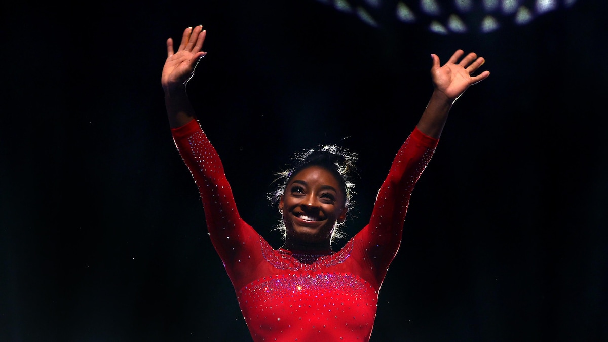 Une gymnaste lève les bras au ciel en souriant.