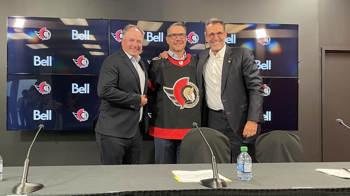 Trois hommes sont tout sourire à la présentation d'un nouvel employé dans un club de hockey professionnel.