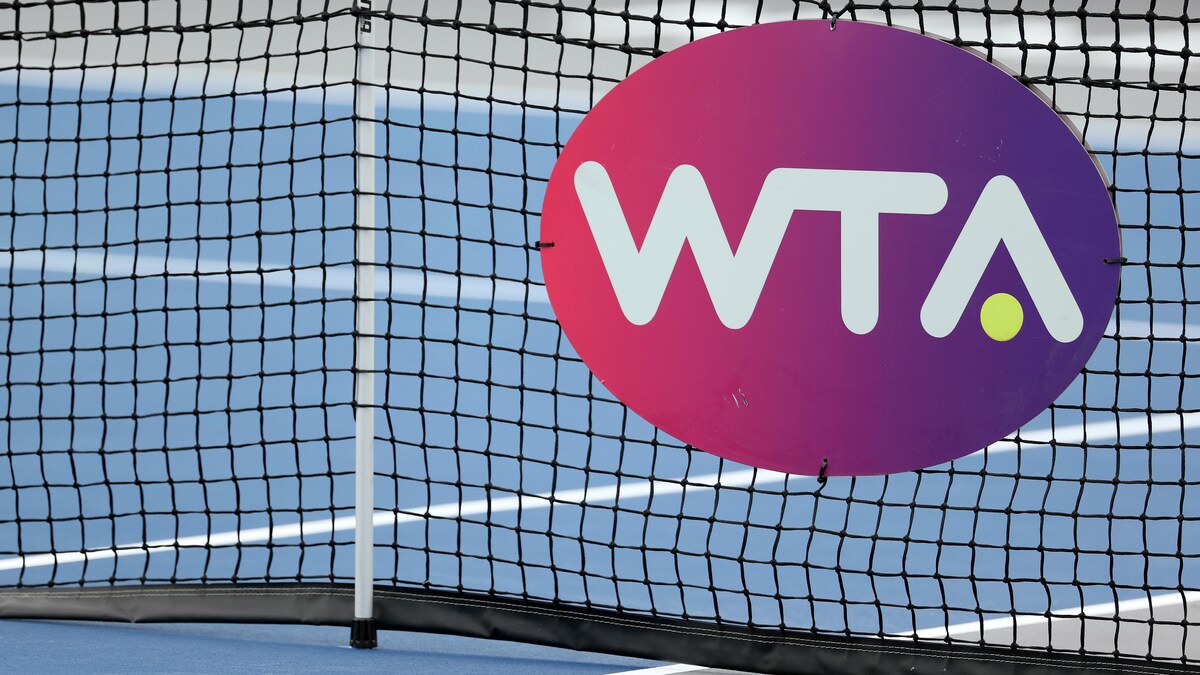 Les lettres WTA écrites en blanc sur un fond rose et mauve et fixées à un filet de tennis.