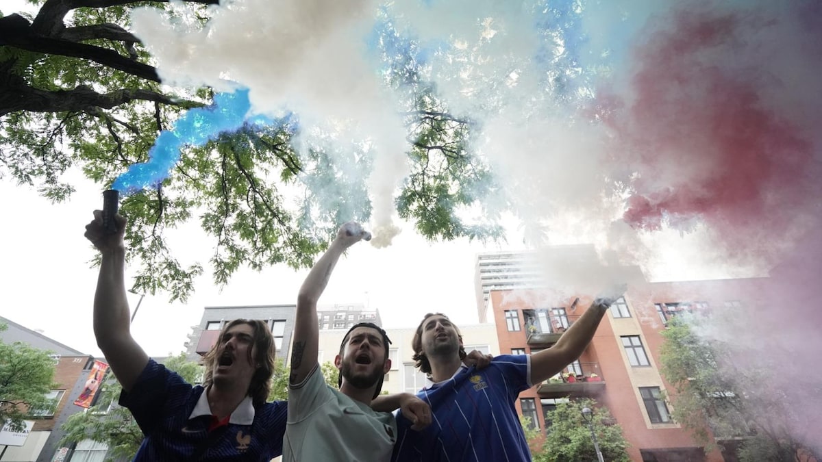 Trois partisans, portant les couleurs de l'équipe de France, brandissent des fumigènes.