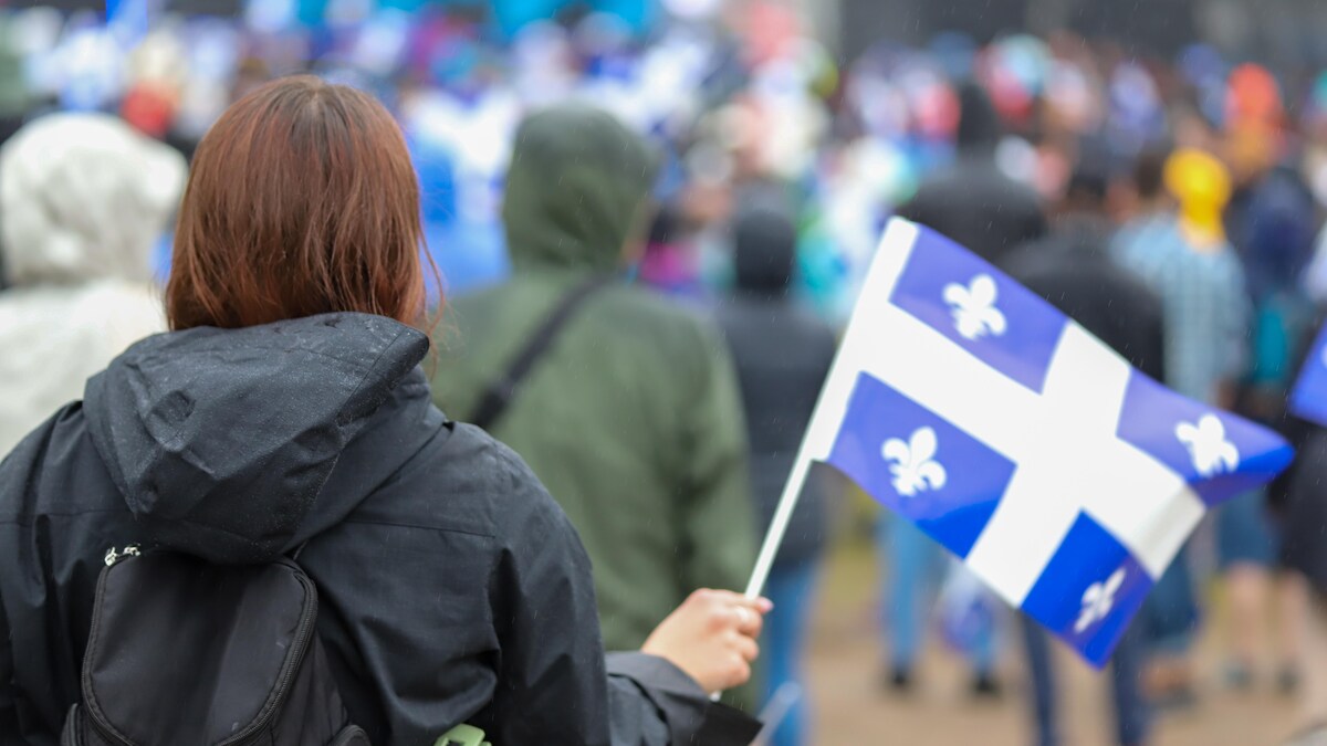 Une femme vue de dos, portant un drapeau du Québec.