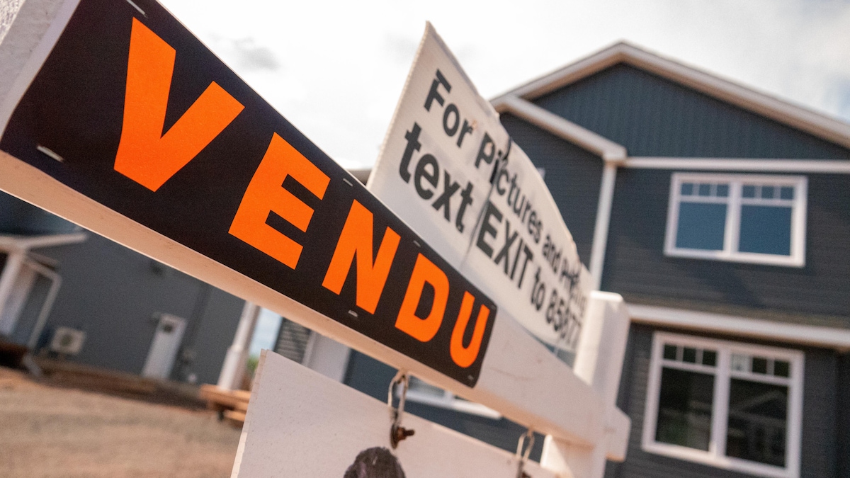 Affiche noire sur laquelle est écrit le mot «Vendu» en lettres orange devant une maison.