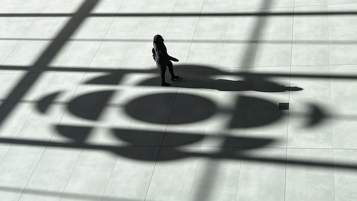 Une personne marche sur l'ombre du logo de Radio-Canada sur le plancher de l'atrium de la Maison de Radio-Canada à Montréal.